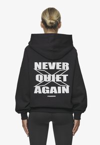 Sudadera negra de gran tamaño con capucha y mangas largas. Presenta un audaz texto blanco "NUNCA CALLADOS DE NUEVO" en la parte posterior, con el nombre de la marca "PEGADOR" debajo.