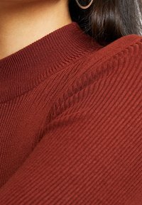 Żebrowany, bordowy materiał z wysokim dekoltem, eksponujący subtelną teksturę i detale wzornicze na górnej części odzieży.