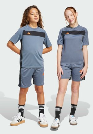 Conjunto atlético gris con acentos naranjas. Camiseta de manga corta y pantalones cortos, de tela de poliéster, con rayas negras. Zapatillas con detalles en blanco y negro.