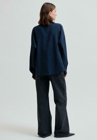 Laivansinis iso koko paita pitkilla hihoilla, hieman pidempi takasivu; yhdistetty korkeavyötäröisiin, leveälahkeisiin tummaan farkkuihin.