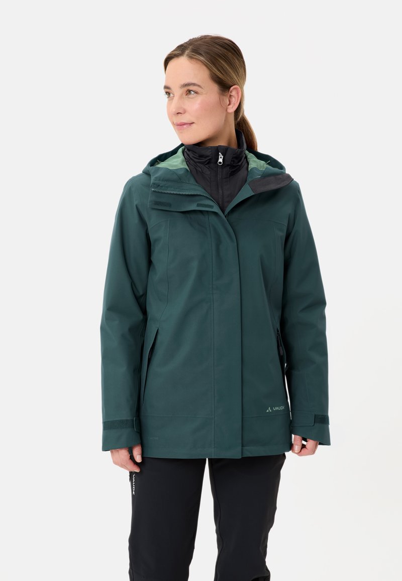 Giacca verde impermeabile con cerniera frontale, cappuccio regolabile e tasche visibili. Include uno strato interno nero e dettagli in tessuto testurizzato.