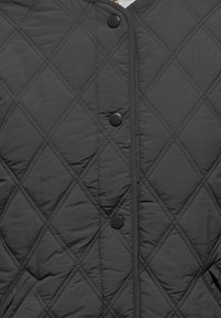 Veste noire matelassée avec un motif en losanges, dotée de grands boutons pression noirs et d'une texture lisse légèrement brillante.