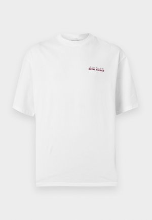 T-shirt blanc à manches courtes avec col rond, petit texte rouge "Royal Palace" sur le côté gauche de la poitrine.