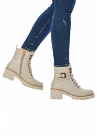 Bottines en cuir beige avec un laçage sur le devant, fermeture éclair sur le côté, talon épais et détail en boucle. Tige texturée et semelle robuste pour une meilleure adhérence.