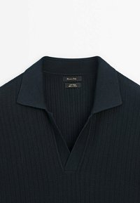 Polo en maille côtelée noire avec col ouvert et étiquette de marque « Massimo Dutti » à l'intérieur du col.
