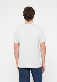 Λευκό βαμβακερό t-shirt με στρογγυλή λαιμόκοψη και κοντά μανίκια. Η πλάτη έχει λεία υφή χωρίς ορατά σχέδια ή διακοσμητικά στοιχεία.