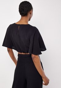 Top corto nero con maniche a sbuffo, tessuto texture, dettaglio a chiave sulla schiena, abbinato a un pantalone a vita alta coordinato.