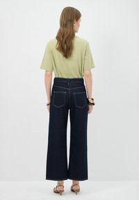 T-shirt verde a maniche corte abbinato a jeans a gamba larga scuri a vita alta con tasche posteriori e dettagli di cucitura bianca.