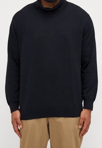 Pull à col roulé bleu marine foncé, fabriqué en tissu doux, doté de poignets et d'un ourlet côtelés, avec une coupe décontractée et un design sans coutures.