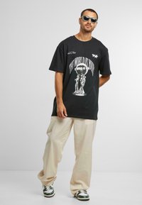 T-shirt noir surdimensionné avec un imprimé graphique disant "LE MONDE EST À VOUS" en blanc. Coupe décontractée, associé à un pantalon beige ample.