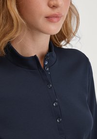 Navyblauwe, langverwarmde shirt met hoge kraag, voorzien van een knoopsluiting en een contrasterende binnenprint zichtbaar bij de hals.