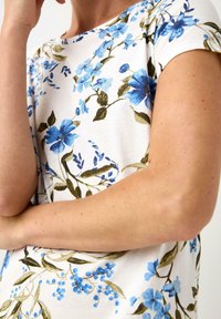 T-shirt i bomull med vit bakgrund, prydd med blommönster i blått och gröna blad; korta ärmar och rundad halsringning.