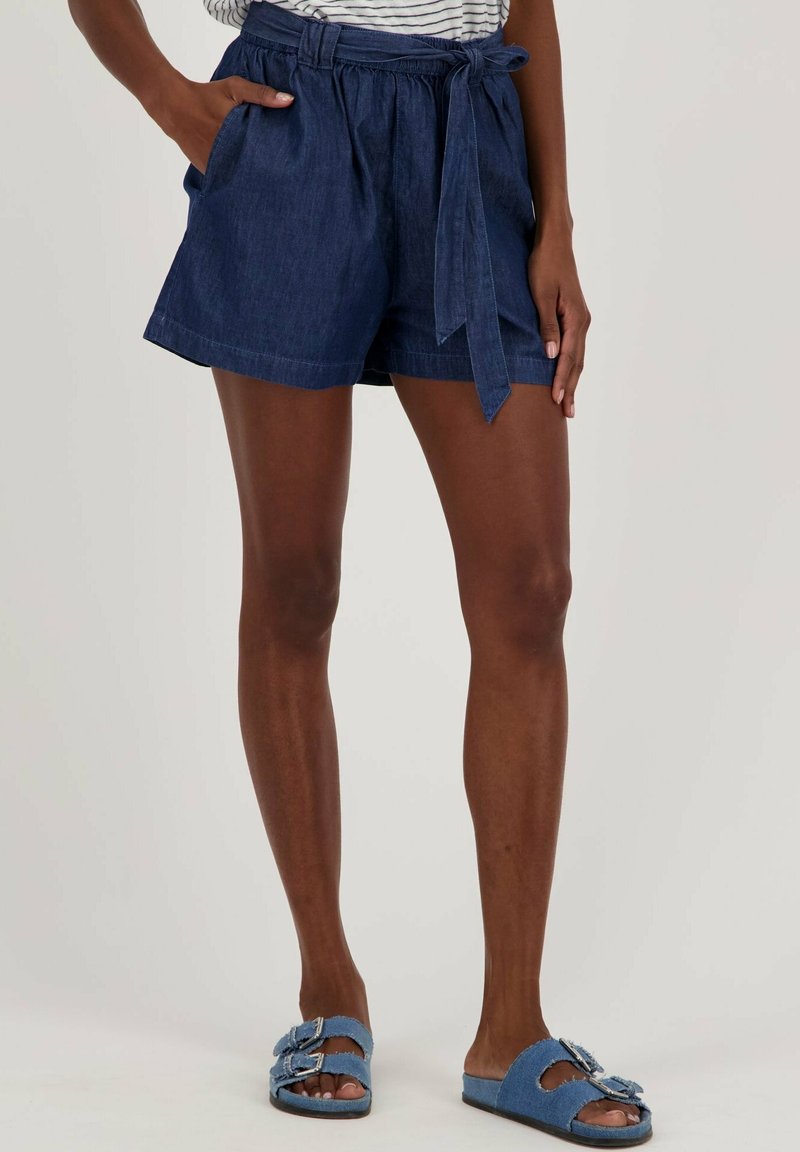 Pantalones cortos de mezclilla con cintura alta, cinturón anudado y bolsillos laterales. Textura suave, color azul oscuro, estilo casual y abertura de pierna ligeramente acampanada.