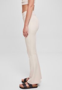 Beige utsvängda leggings i mjukt, stretchigt tyg, med hög midja, tillsammans med kraftiga plattformssandaler i svart och brunt.
