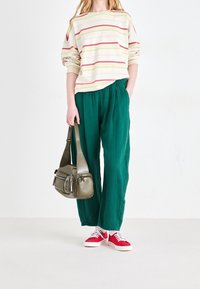 Gestreept shirt met lange mouwen in pasteltinten, gecombineerd met losse groene broek en rode sneakers. Handtas is olijfgroen met meerdere vakken.