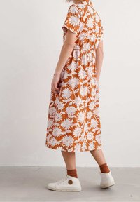 Brown floral dress with white daisy patterns, short sleeves, gathered waist, and knee-length hem, paired with white sneakers and brown socks.