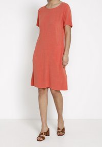 Koral kortärmad klänning med rund halsringning, avslappnad passform och mjuk textur; ihop med bruna klacksandaler.