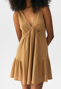 Robe marron sans manches avec un décolleté en V profond, tissu texturé, corsage froncé et ourlet évasé. Design simple et décontracté sans ornements.