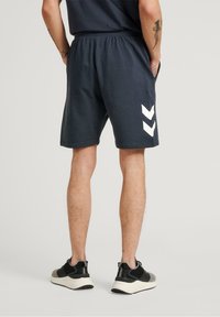 Marina bomullsshorts med elastisk midja, med vita chevron-accenter på sidorna. Löst sittande design, perfekt för avslappnad användning.