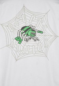 Weißes T-Shirt mit einer grünen Cartoon-Spinne in einem Netz, mit schwarzen Akzenten auf der Spinne und grauen Linien des Spinnennetzes. Der Text lautet "CREEPY".