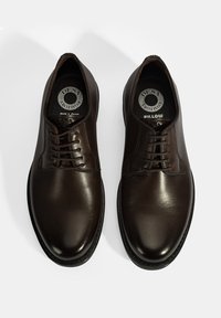 Bruine leren veterschoenen met een gladde textuur, ronde neus en zwarte rubberen zool. Kenmerkt zich door branding op de binnenzolen en eenvoudige stiksels.