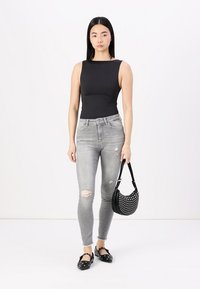 Top sans manches noir, jean skinny gris déchiré et sac à main noir à pois. Chaussures plates noires avec des détails en nœud. Fond blanc.