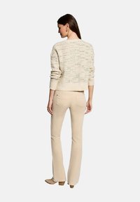 Un pull en tricot de couleur crème avec un motif texturé, associé à un pantalon évasé beige clair, vu de dos.