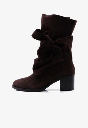 Bottine en daim marron avec un revers plié et un grand nœud décoratif, dotée d'un talon épais noir et d'une texture lisse.