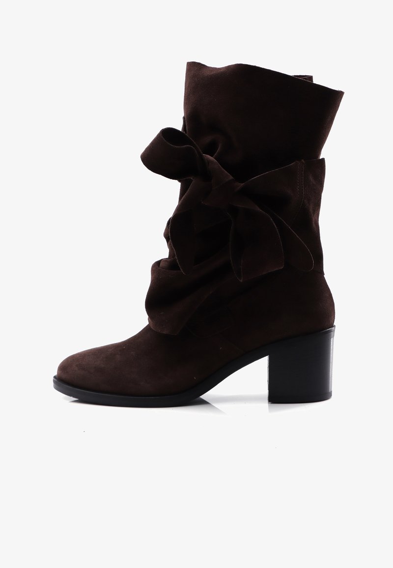 Botín de ante marrón hasta el tobillo con un puño doblado y un gran detalle de lazo, con un chunky tacón negro y una textura suave.
