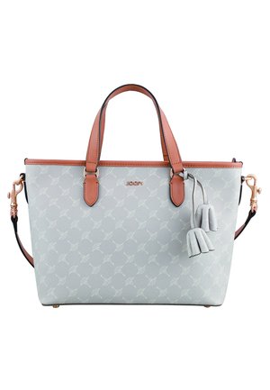 Sac à main gris clair à motifs, avec des anses couleur tan, une bandoulière amovible et deux breloques pompons suspendues près du bord supérieur.