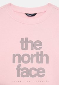 Rózsaszín pulóver bordás nyakkal, melyen a "the north face" felirat szürke színben, jól láthatóan szerepel, alatta pedig a "NEVER STOP EXPLORING" szöveg található.