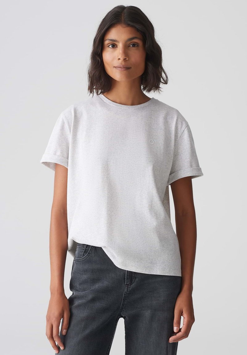 Lichtgrijs t-shirt met korte mouwen en een ronde hals, gemaakt van zachte stof, met een klein logo op de linkerborst. Gecombineerd met donkere spijkerbroeken.