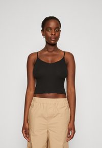 Čierny rebrovaný crop top s tenkými ramienkami, s vlnitým výstrihom a priliehavým strihom, skombinovaný s béžovými nohavicami na elastický pás.