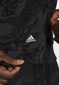 Maglietta sportiva nera con un motivo testurizzato, orlo a costine e una patch con il logo Adidas in bianco su uno sfondo scuro.