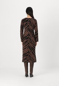 Vestito a maniche lunghe, aderente, con un motivo zebra in nero e marrone, realizzato in tessuto a maglia, che arriva a metà polpaccio, abbinato a stivali alti marroni con tacco.