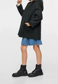 Mörkgrå ullkappa med huva, oversized passform, knappstängning, två fickor; blå denimkjol med utsvängd nederdel; svarta snörstövlar med tjocka sulor.