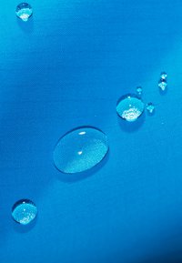 Blauer Stoff mit strukturierter Oberfläche, auf dem mehrere klare Wassertropfen in verschiedenen Größen ruhen.