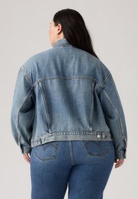 Light blue denim jacket features a relaxed fit, classic collar, and button closures, with visible stitching and back yoke details.
