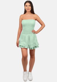 Mintgroene strapless jurk met een smock-borsten en een rucheszoom, gemaakt van textuurstof, gedragen met witte sneakers.