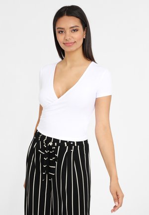 Witte T-shirt met korte mouwen en V-hals, met een aansluitende pasvorm, gecombineerd met zwart-witte gestreepte high-waisted broek met een strikdetail in de taille.