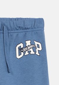 Blaue Baumwoll-Sweathosen mit elastischem Bund, versehen mit einem kontrastierenden weißen "GAP"-Logo und einem geschwungenen "Hot Wheels"-Design.