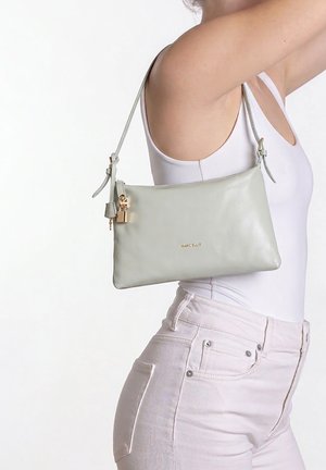 Femme portant un débardeur blanc et un jean rose clair porte un sac bandoulière gris clair Marc Ellus avec un détail de serrure dorée.
