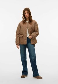 Bruine gewatteerde jas met een ronde kraag, voorste knopen en zijzakken; gedragen over een witte top en gecombineerd met blauwe jeans en bruin schoenen.