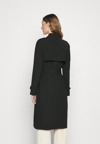 Svart trenchcoat med belte i midjen, laget av et glatt stoff, med bred krage og lagdelt bakdesign.