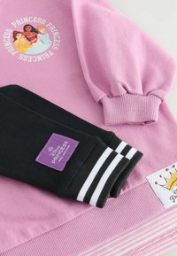 Sweat-shirt rose avec des manches bouffantes, poignets côtelés noirs avec des rayures blanches et un graphique de princesse Disney. Comprend une étiquette violette.