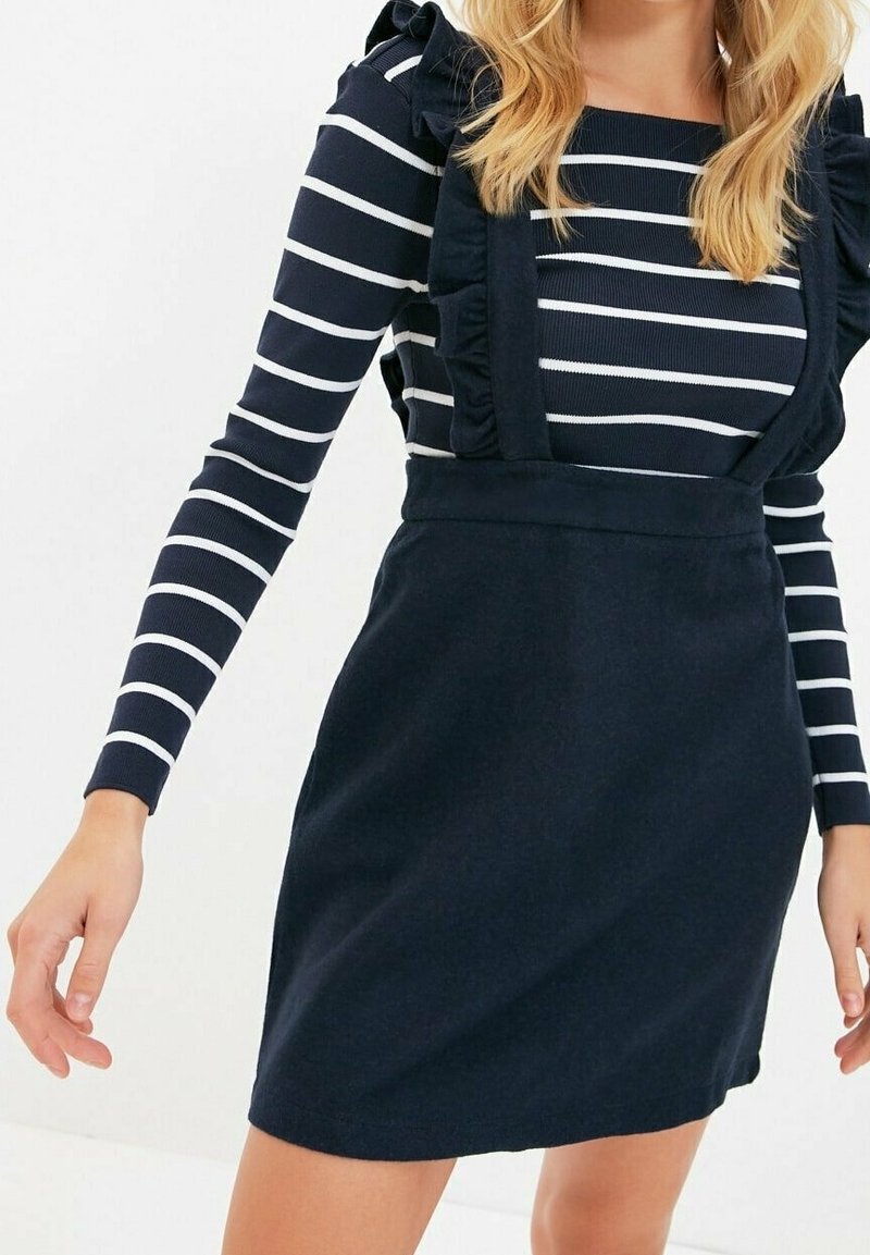 Robe bleu marine avec des bretelles à volants sur un haut rayé bleu et blanc à manches longues. Texture douce, design ajusté, longueur genoux.