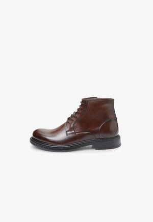 Stivale ankle in pelle marrone con finitura liscia, chiusura con lacci, punta rotonda e suola in gomma nera. Semplice dettaglio di cucitura lungo i bordi.