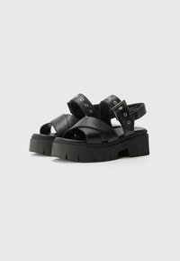 Black platform sandals with wide crisscross leather straps, adjustable ankle buckle, and textured rubber sole with deep grooves for grip.