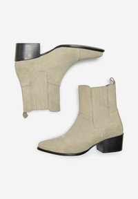 Botines de ante beige con punta afilada, tacón negro apilado y detalles de costura vertical en los laterales. Incluyen lazos para facilitar el calzado.