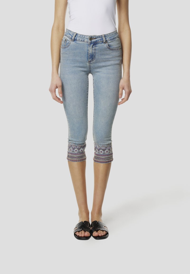 Hellblaue Capri-Jeans mit dekorativen bestickten Bündchen in Lila und Grau. Verfügt über eine figurbetonte Passform und ein Fünf-Taschen-Design.